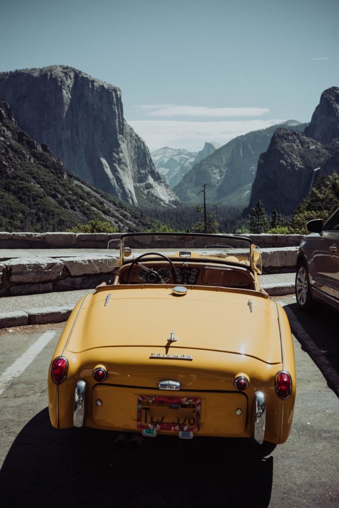 Parked yellow convertible overlooking a mountain view.