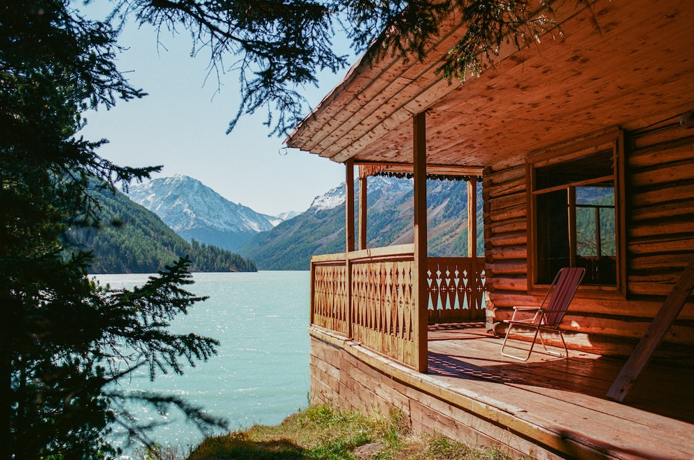 wooden cabin overlooking a blue lake with a mountain landscape behind