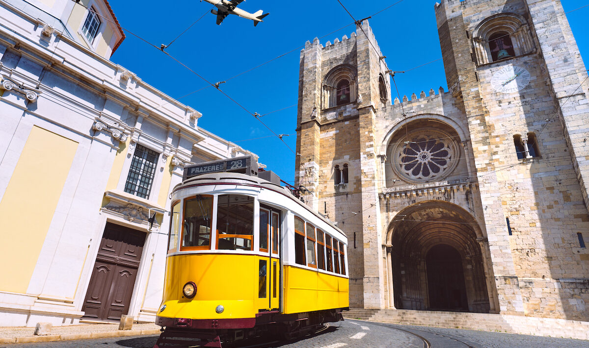 Yellow tram in Lisbon with a plane flying in the blue sky