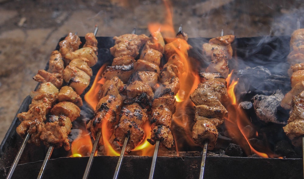 meat being grilled on skewers over hot coals on a bbq.