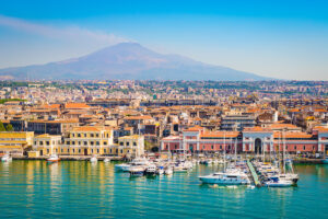 Catania Sicily port with orange roofed buildings and boats docked in blue sea
